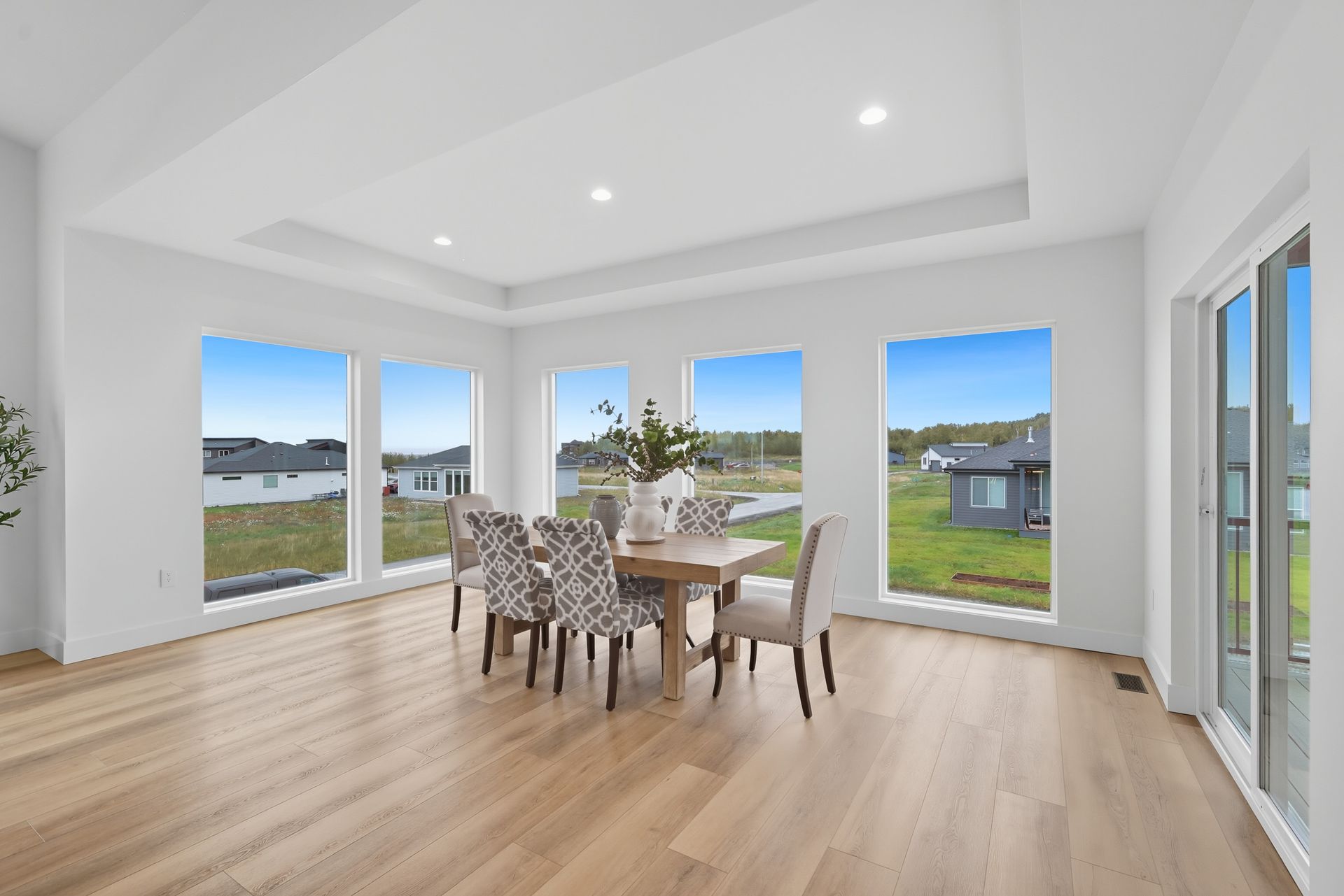 Bright open dining room with light wood floors, large windows, and a table with patterned chairs