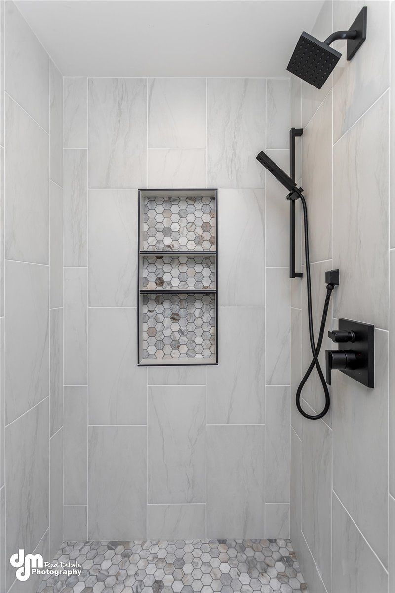 Tiled walk-in shower with black fixtures, overhead rain shower, handheld spray, and recessed niche.