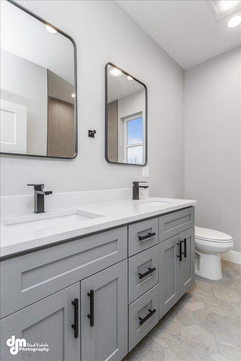 Modern gray bathroom vanity with double mirrors, white countertop, and toilet in a bright, tiled room