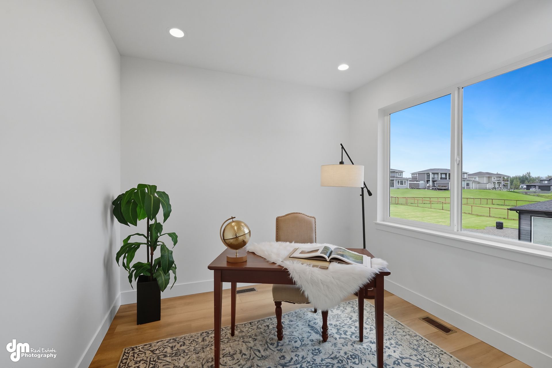 Bright home office with desk, chair, floor lamp, plant, and large window overlooking a green field.