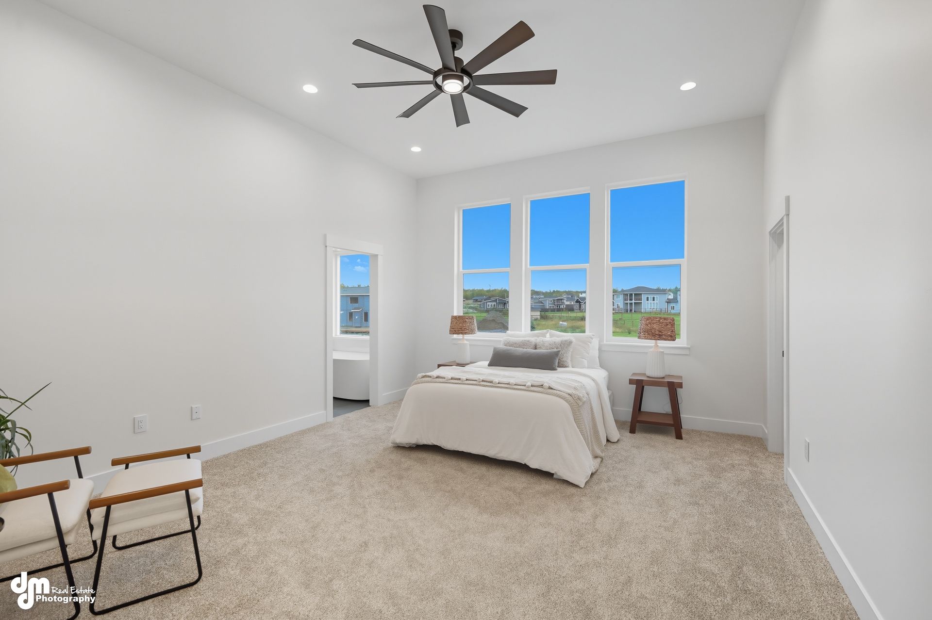 Bright minimalist bedroom with white walls, large windows, bed, chair, and ceiling fan