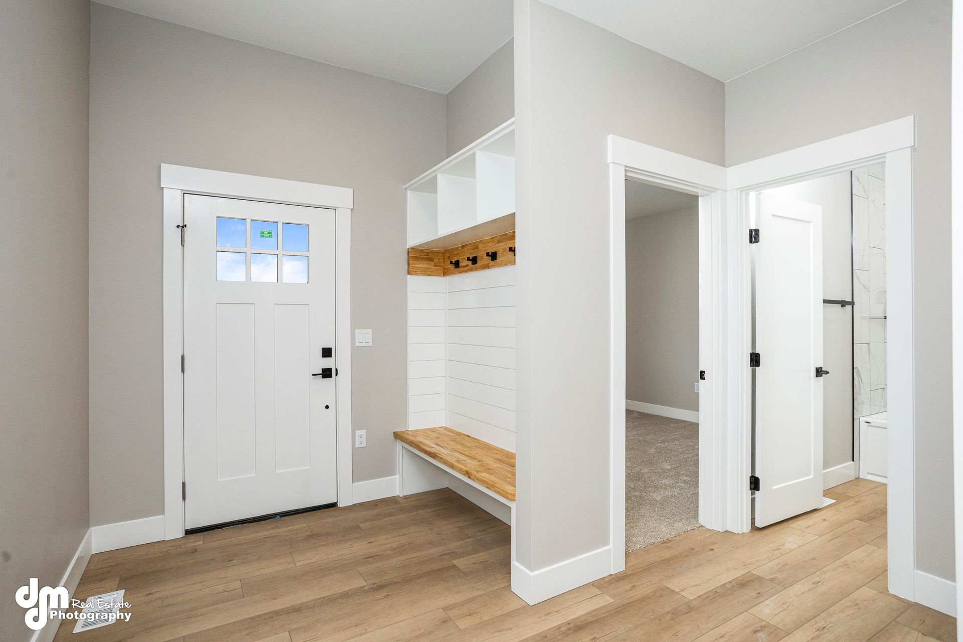 Bright mudroom with white door, bench, coat hooks, and light wood floors