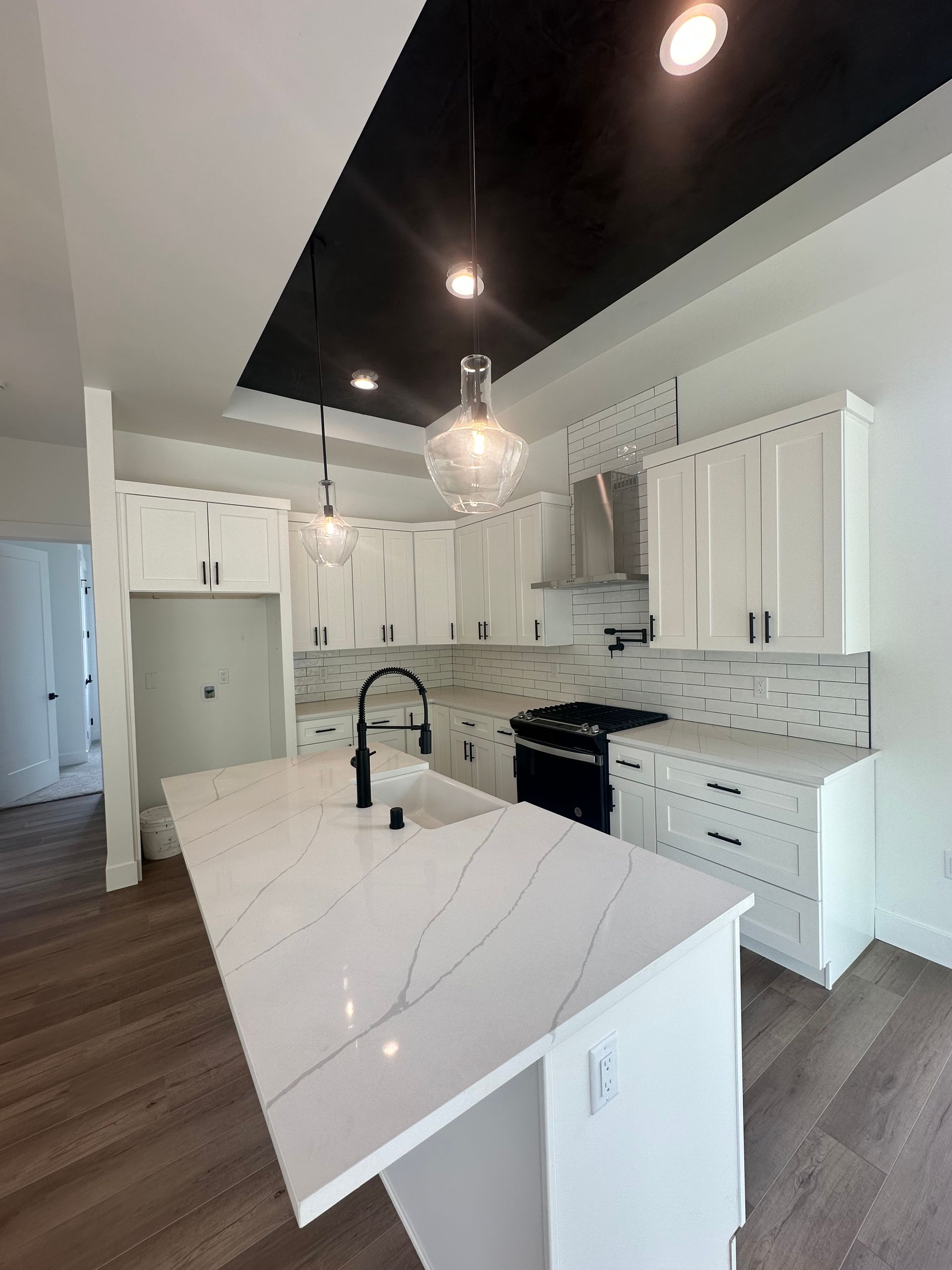 Modern white kitchen with large marble island, black faucet, pendant light, and dark wood floors