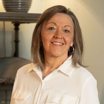Woman with short gray hair smiles in a white collared shirt, indoors.