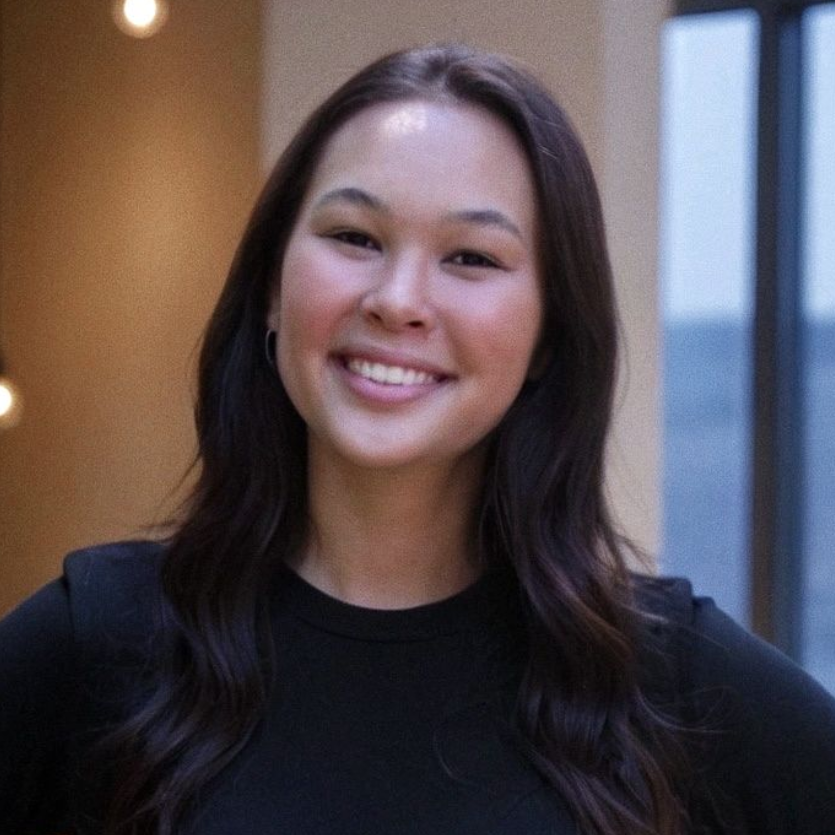 Smiling person with dark hair in a black top, indoors.