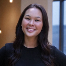 Smiling person with dark hair in a black top, indoors.