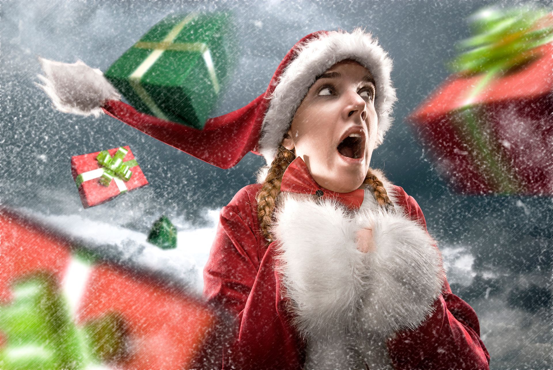 Woman in Santa suit with mouth open, looking up as gifts fly through the snow.