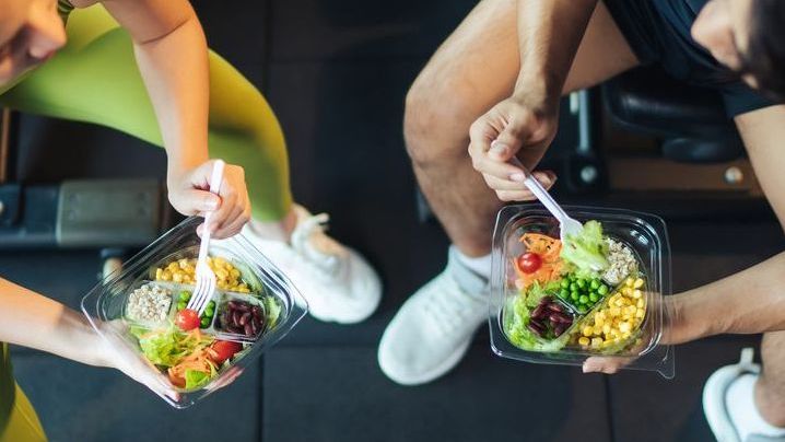 Two people in workout attire eating healthy salads at a gym.