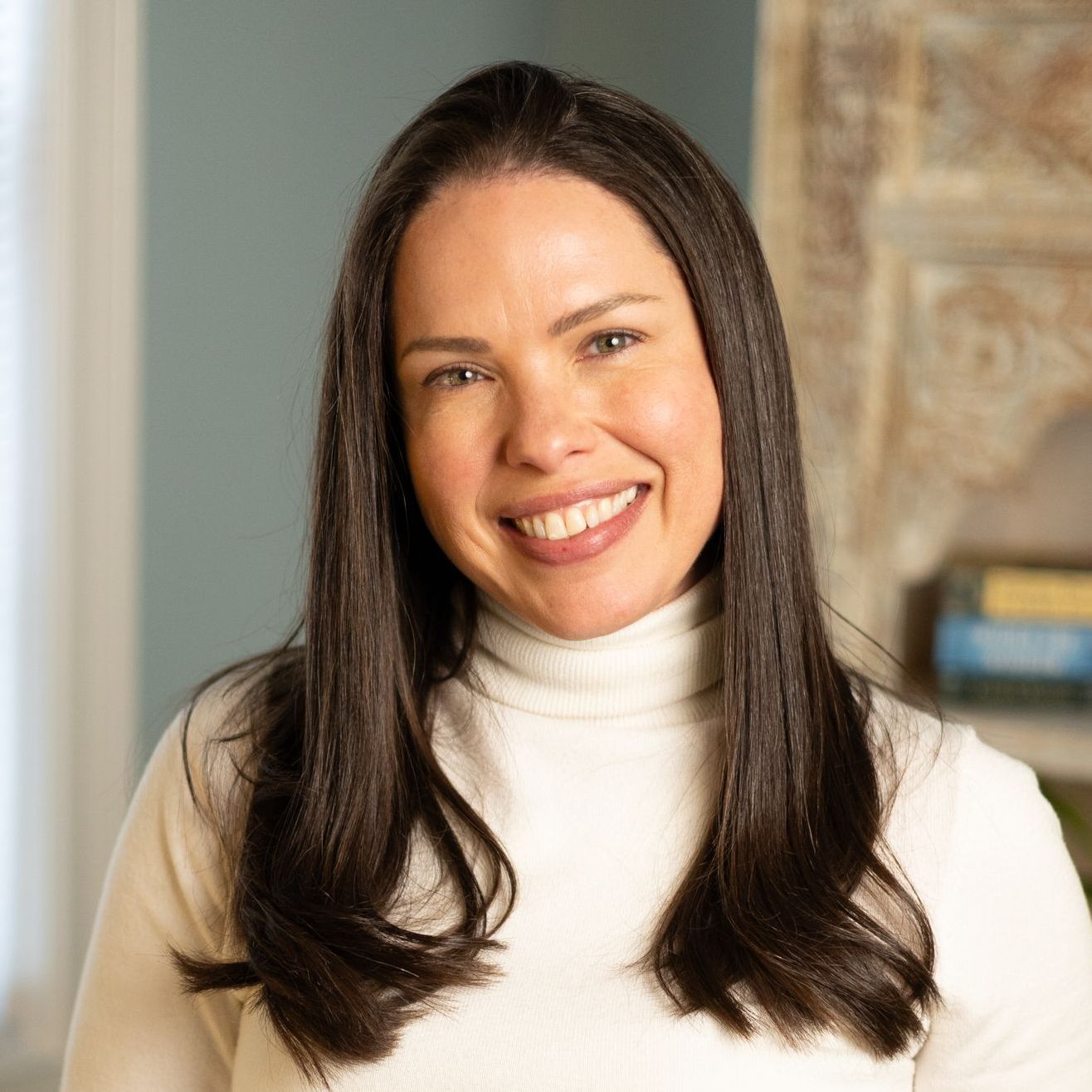 Woman with dark hair, smiling, wearing a white turtleneck sweater.