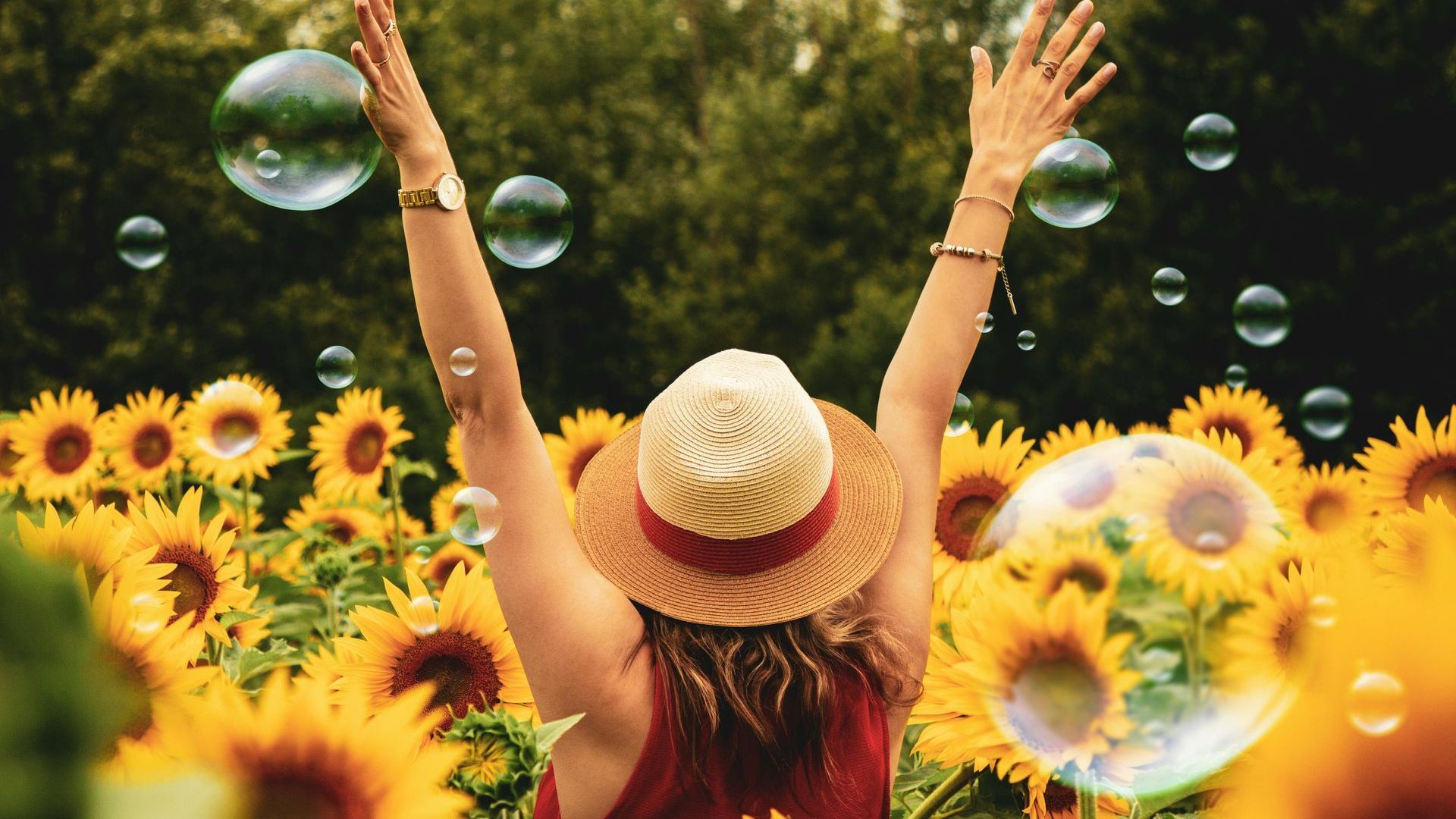Woman with arms raised, in sunflower field, bubbles floating.