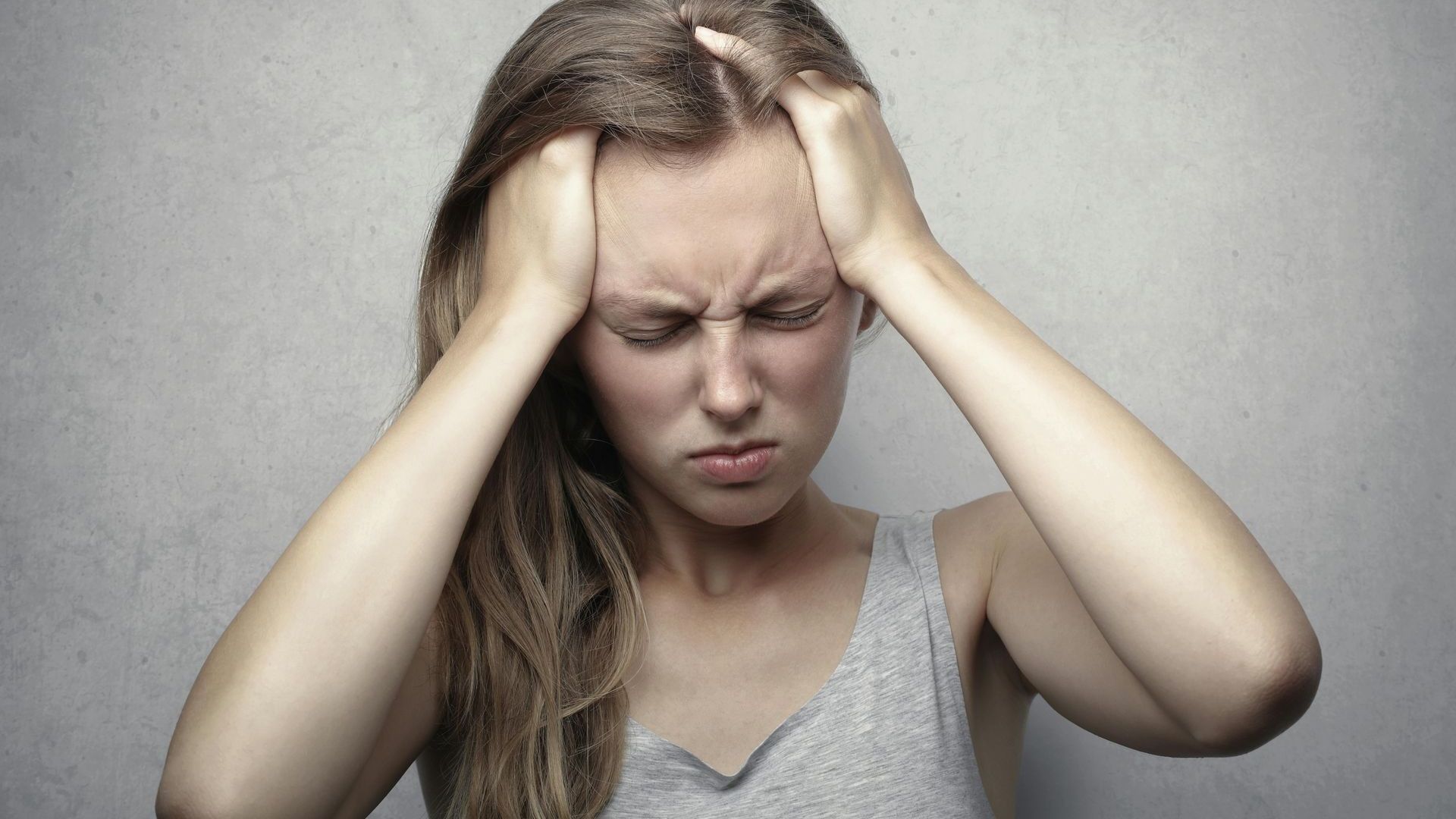 Woman with long brown hair, eyes closed, holding her head, showing distress.
