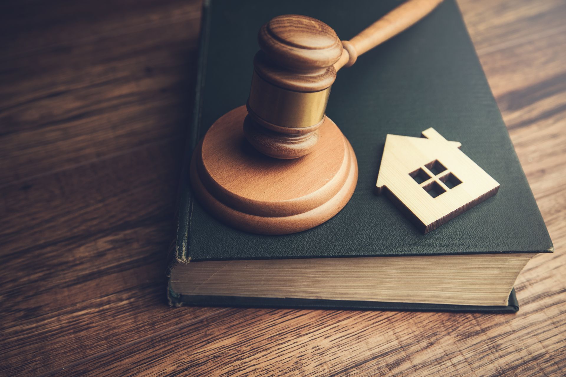 A wooden gavel and small house icon resting on a thick law book on a wooden desk. A wooden gavel and small house icon resting on a thick law book on a wooden desk.