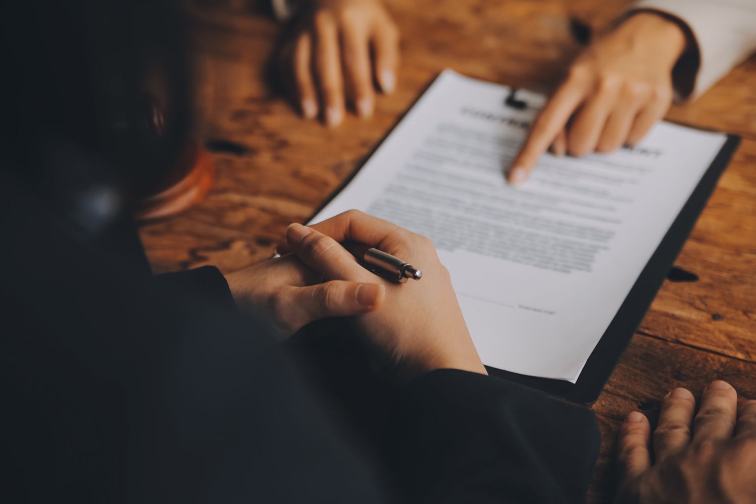 A close-up of a lawyer counseling a client on signing a document on a table. A close-up of a lawyer counseling a client on signing a document on a table.