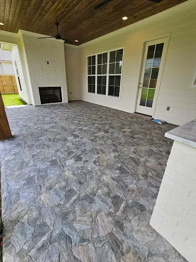 Covered patio with gray patterned flooring, white walls, wood ceiling, fireplace, and glass doors