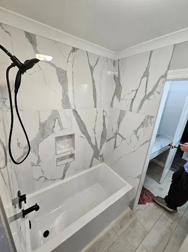 Modern bathroom with white marble-tile walls, black fixtures, and a built-in bathtub/shower stall