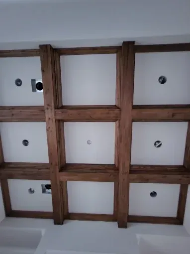 Wooden ceiling grid with recessed lights and white panels in a room interior