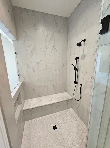 Modern walk-in shower with white marble walls, bench, hex tile floor, and black shower fixtures
