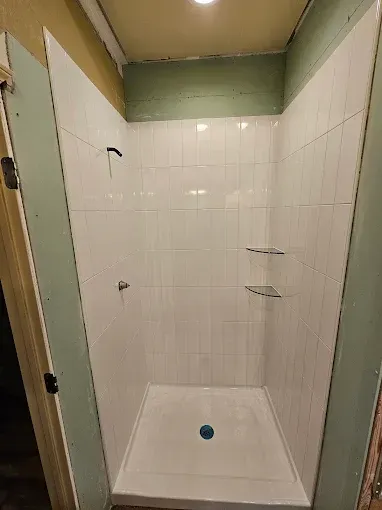 Small tiled shower stall with white walls, green trim, and a blue drain cover.