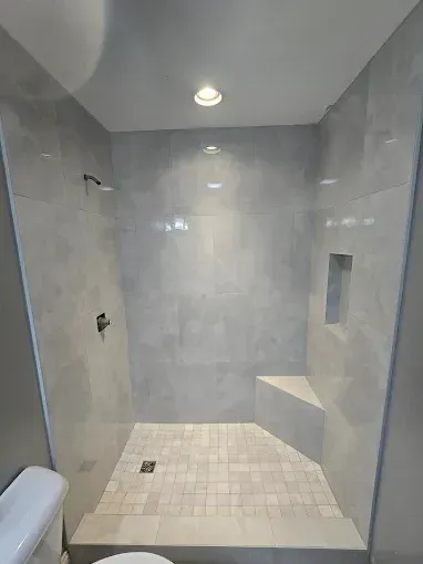 Modern tiled walk-in shower with gray walls, a bench, and a ceiling light
