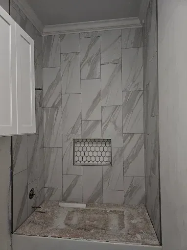 Small bathroom with marble-pattern tile, white cabinet, and unfinished sink counter under a recessed light shelf