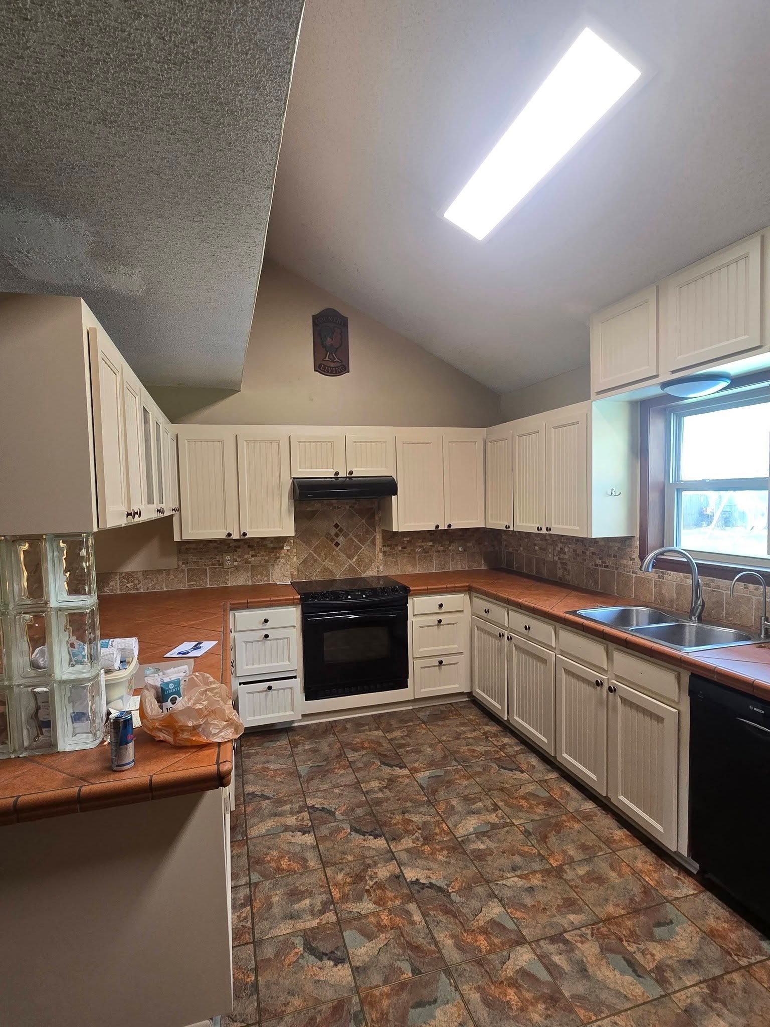 Spacious kitchen with white cabinets, brown countertops, patterned floor, and a large window under bright ceiling lights