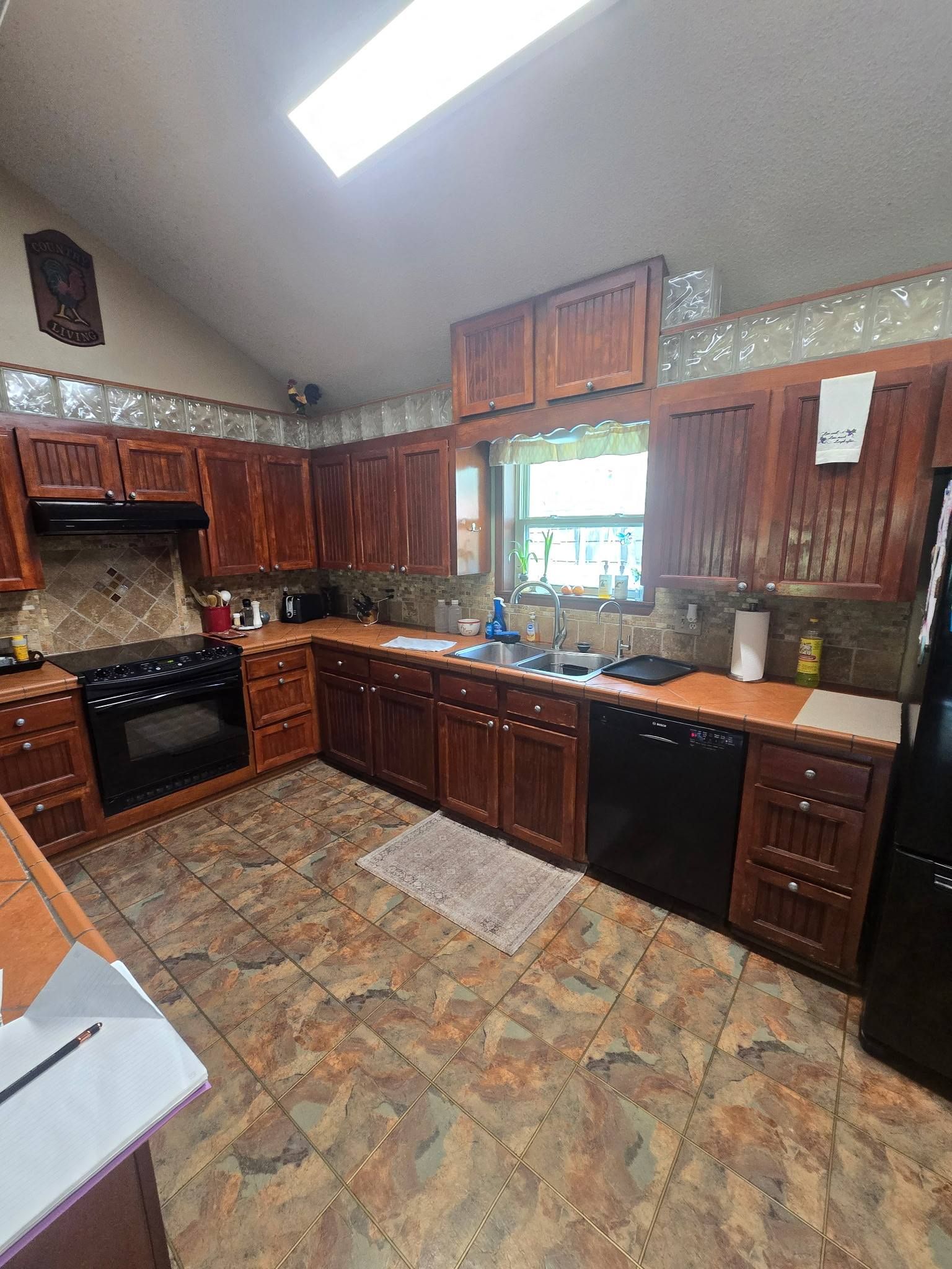 Kitchen with dark wood cabinets, tiled floor, skylight, and window over a sink.
