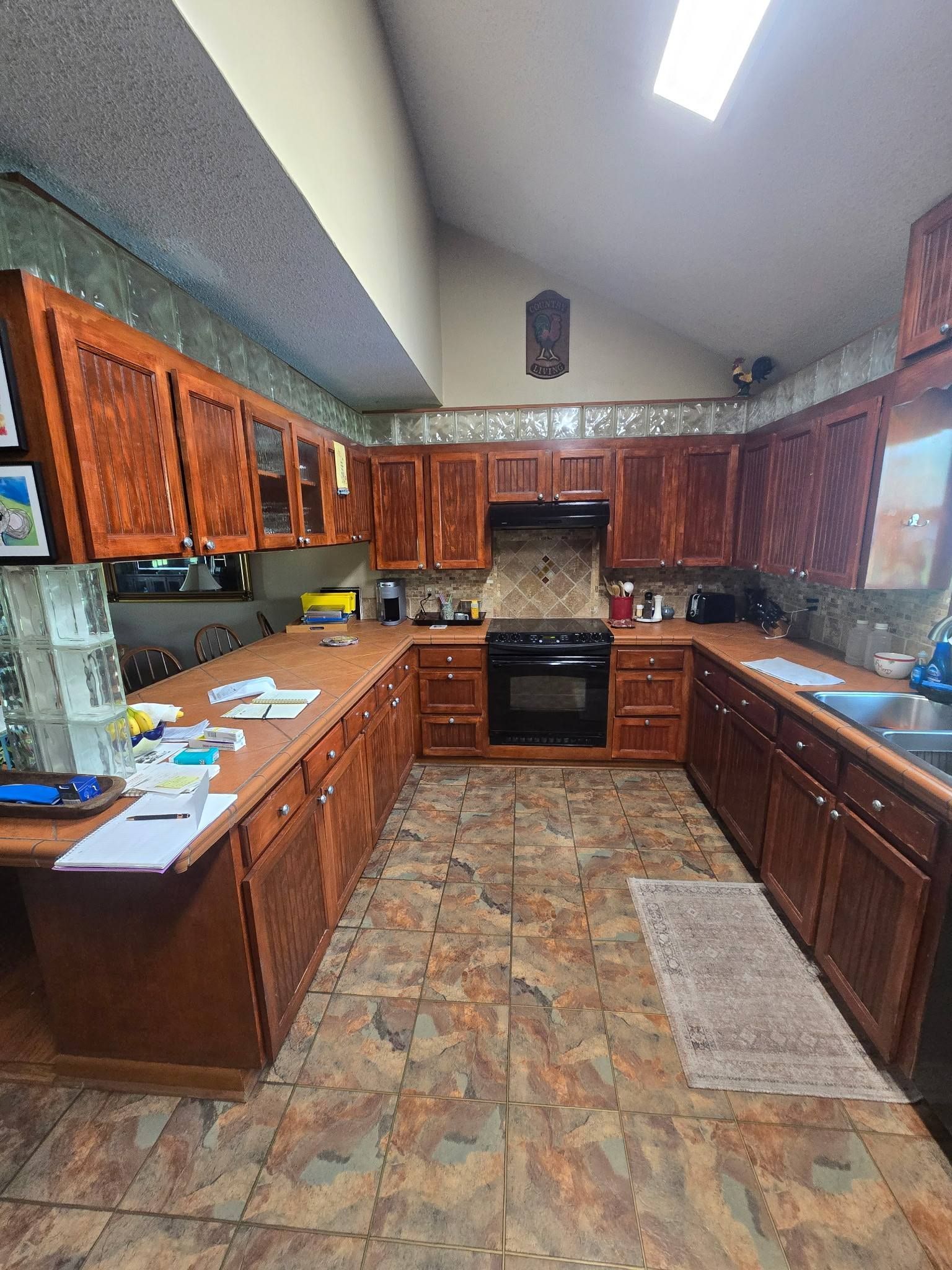 Spacious kitchen with wooden cabinets, tiled floor, black appliances, and a skylight-lit ceiling.