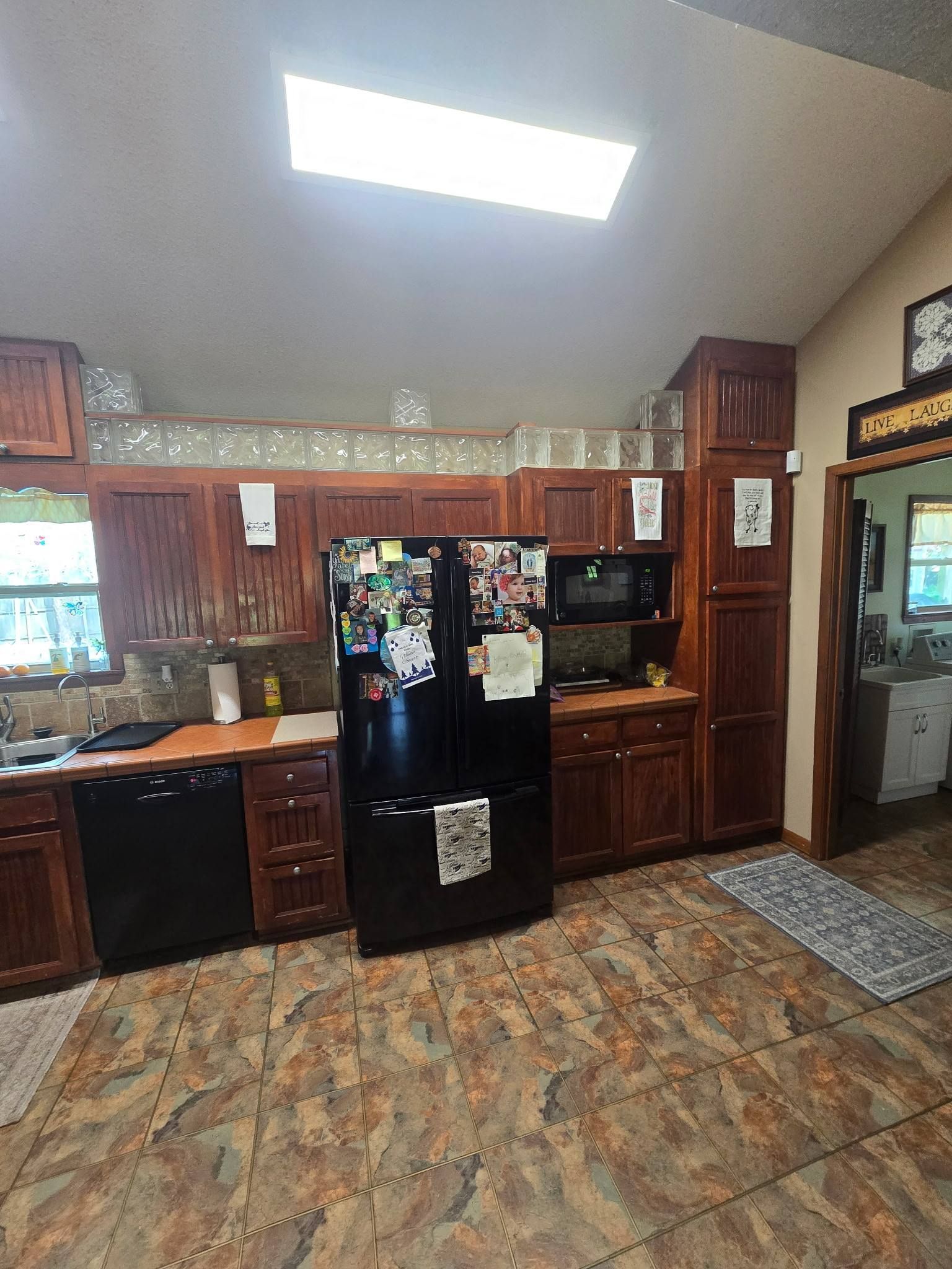 Kitchen with black refrigerator, wooden cabinets, tiled floor, and bright skylight ceiling