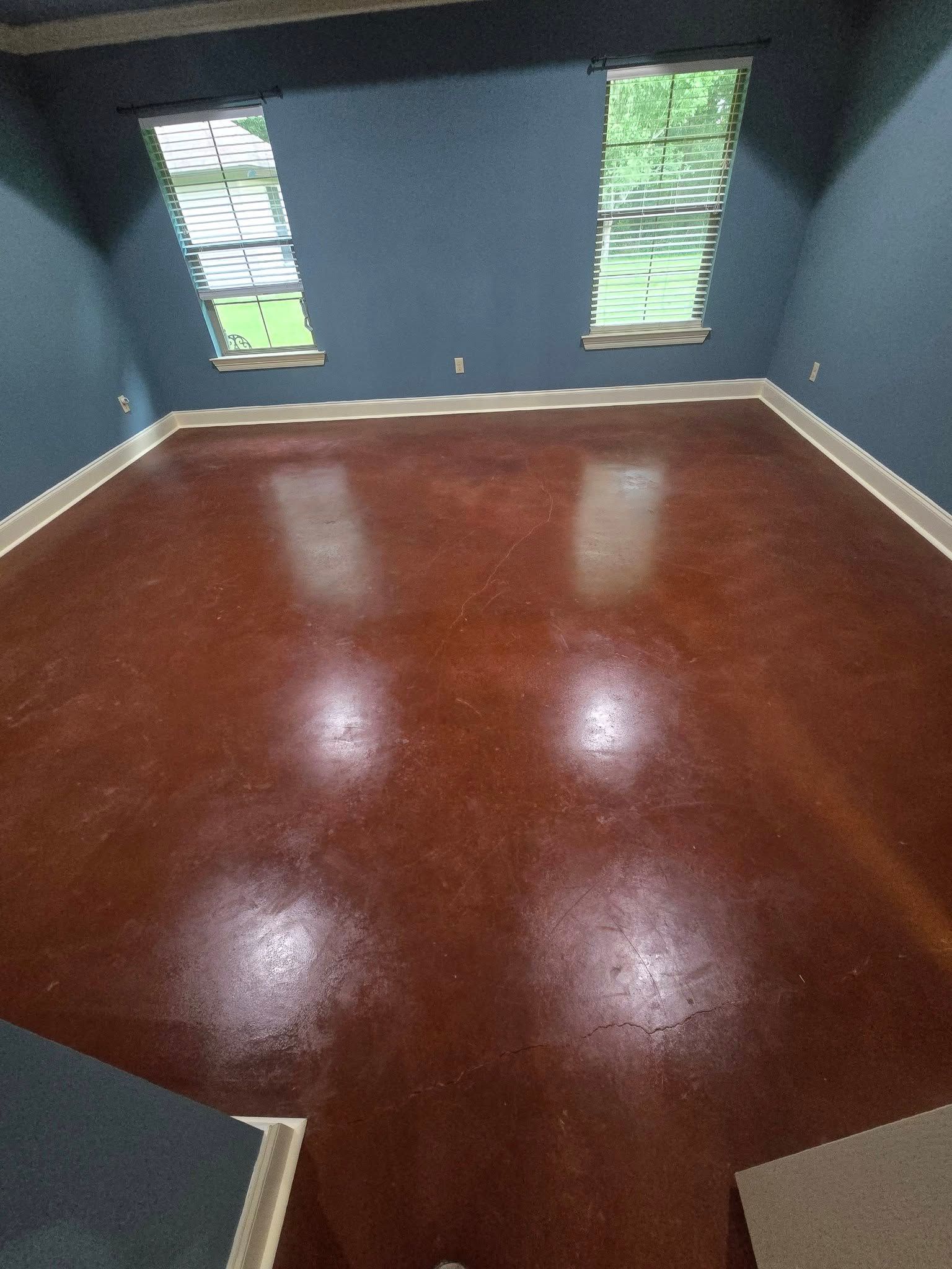 Empty room with dark blue walls, glossy reddish wood floor, and two narrow windows.