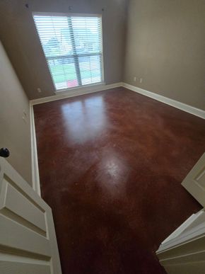 Empty beige room with reddish-brown floor and window blinds letting in daylight