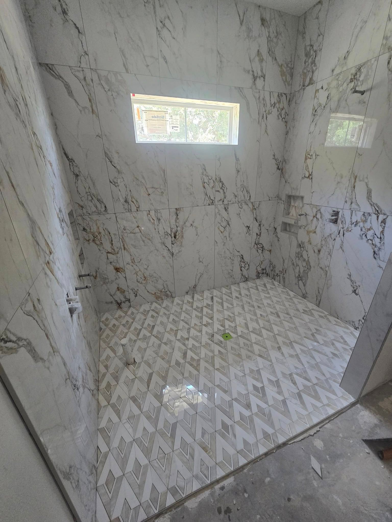Empty tiled shower with marble-look walls, patterned floor, and two small windows.