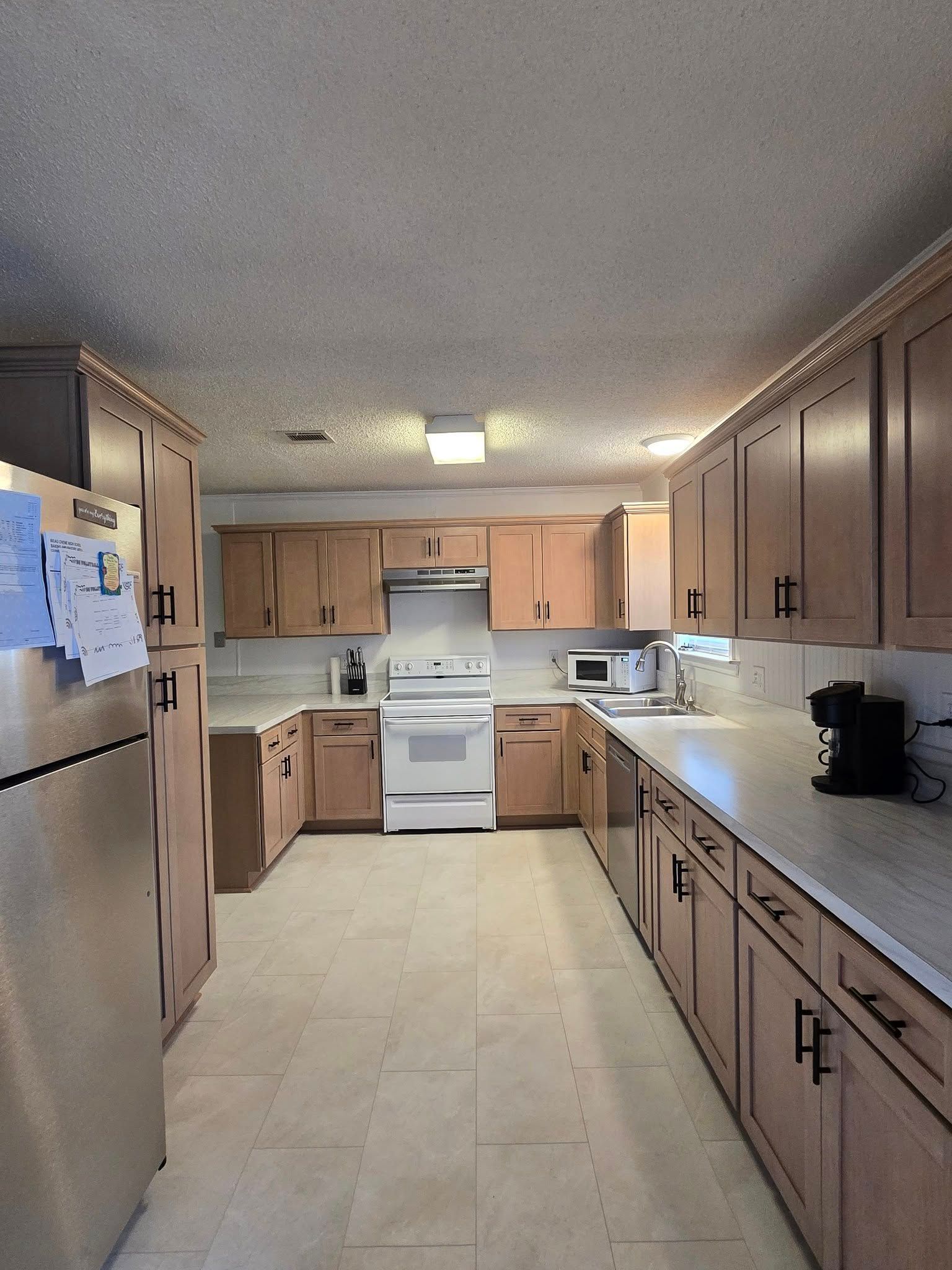 Narrow kitchen with wood cabinets, white appliances, and a bright ceiling light at the far end.