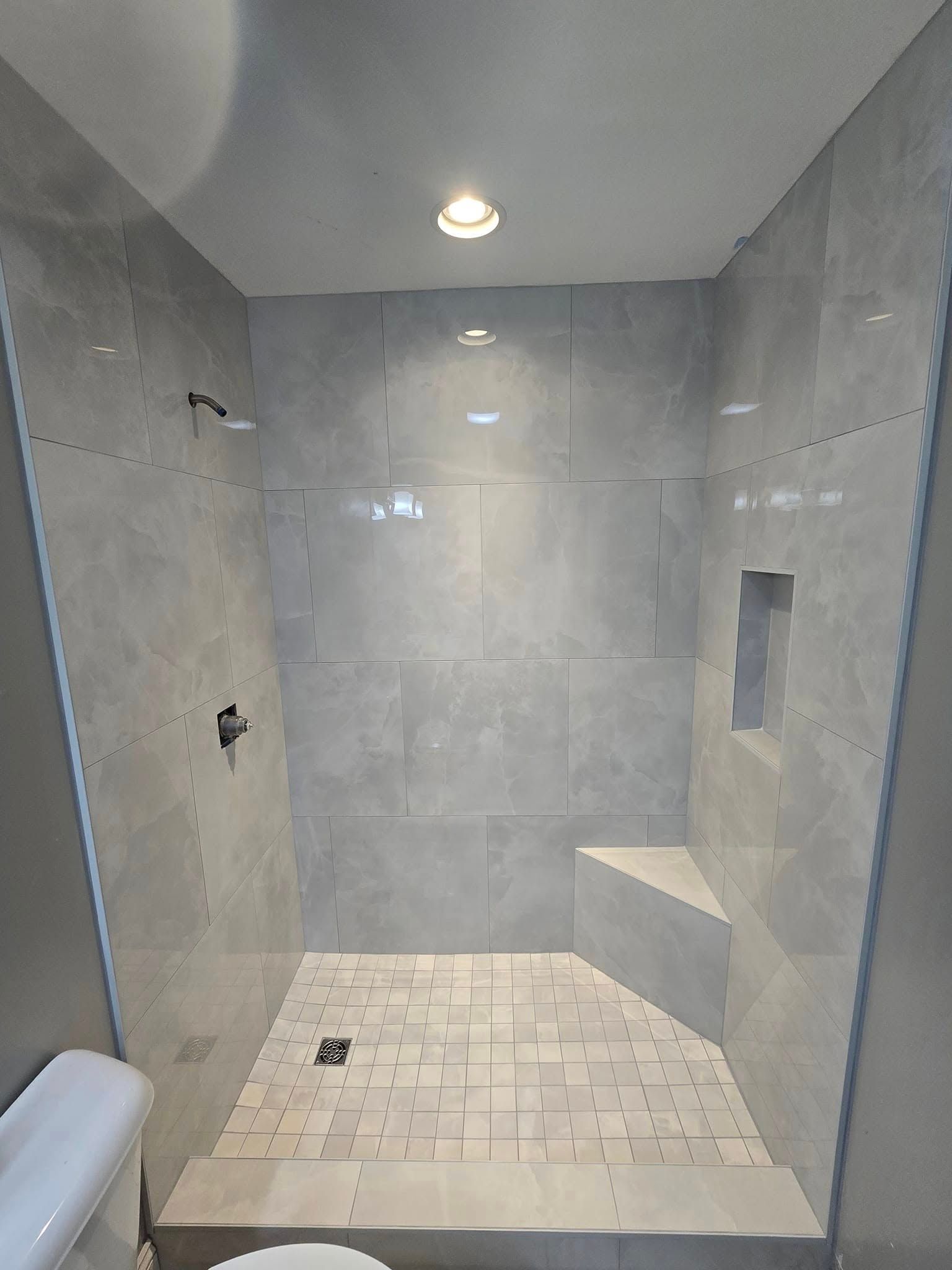 Empty tiled shower with gray walls, bench seat, and recessed light overhead