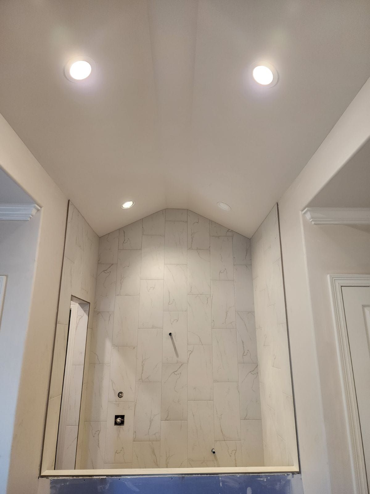 Modern bathroom alcove with marble tile, recessed lights, and a large wall mirror above a tub niche