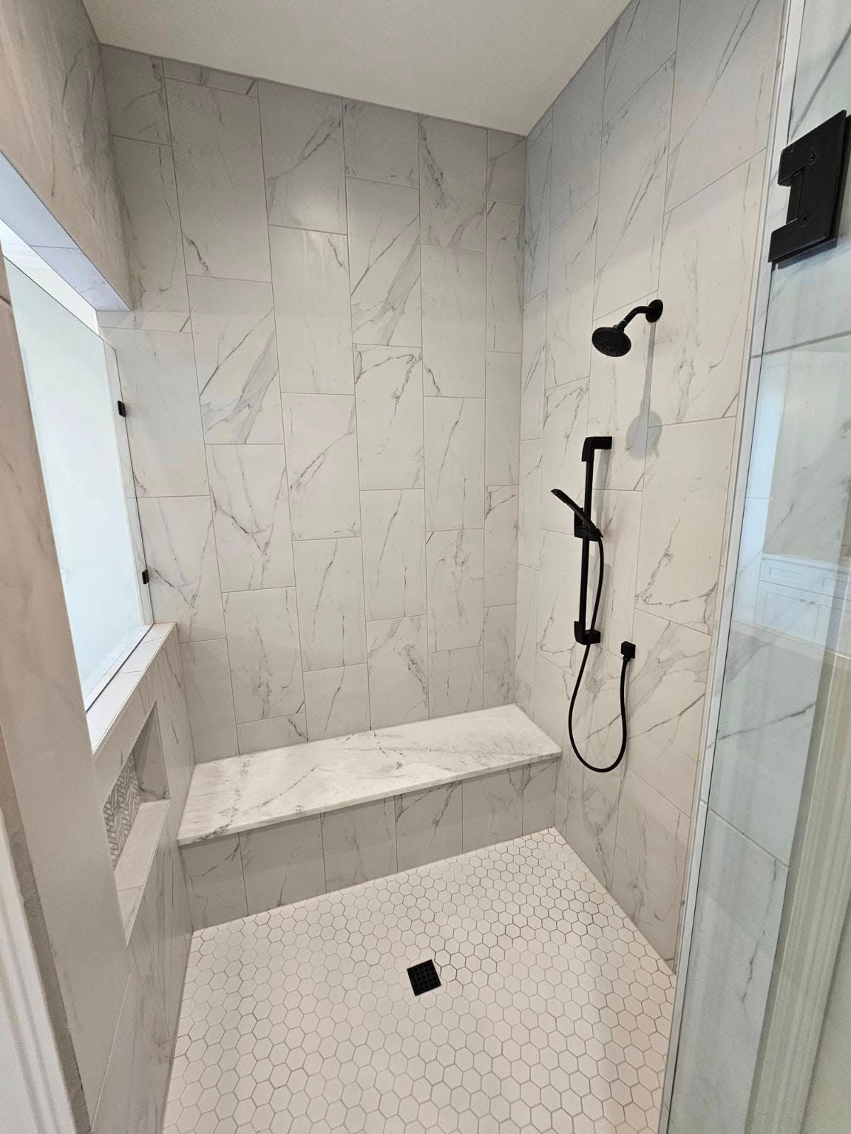 Modern white tiled walk-in shower with built-in bench and black rainfall showerhead
