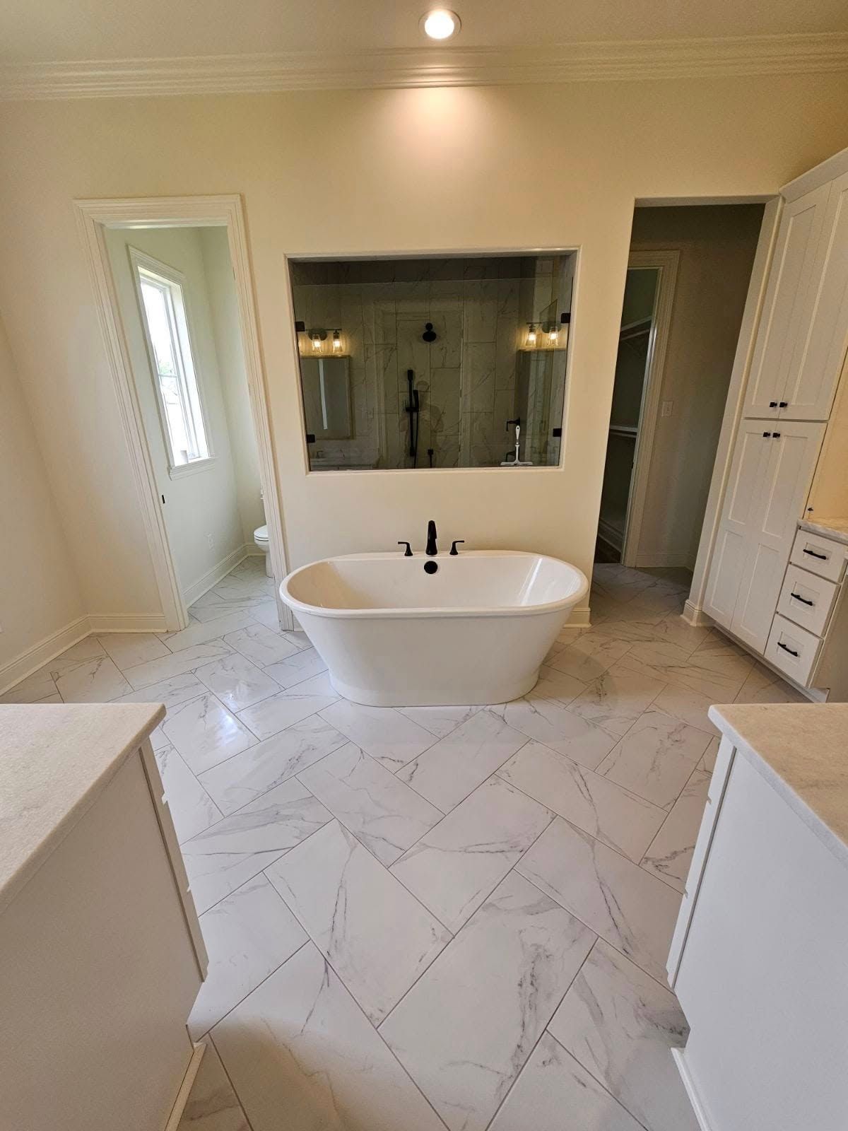 Bright bathroom with freestanding tub, large mirror, white tile floor, vanity, and built-in shelving.