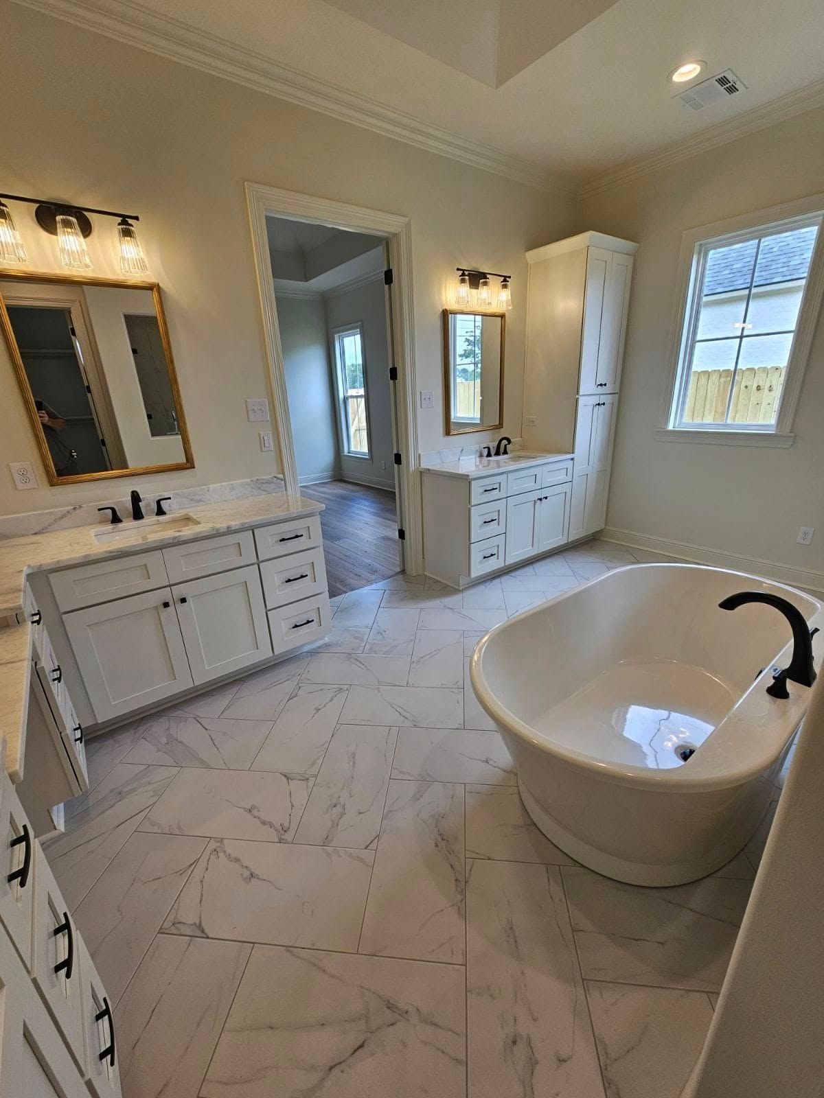 Bright bathroom with freestanding tub, double vanity, large mirror, and white marble-pattern tile floor