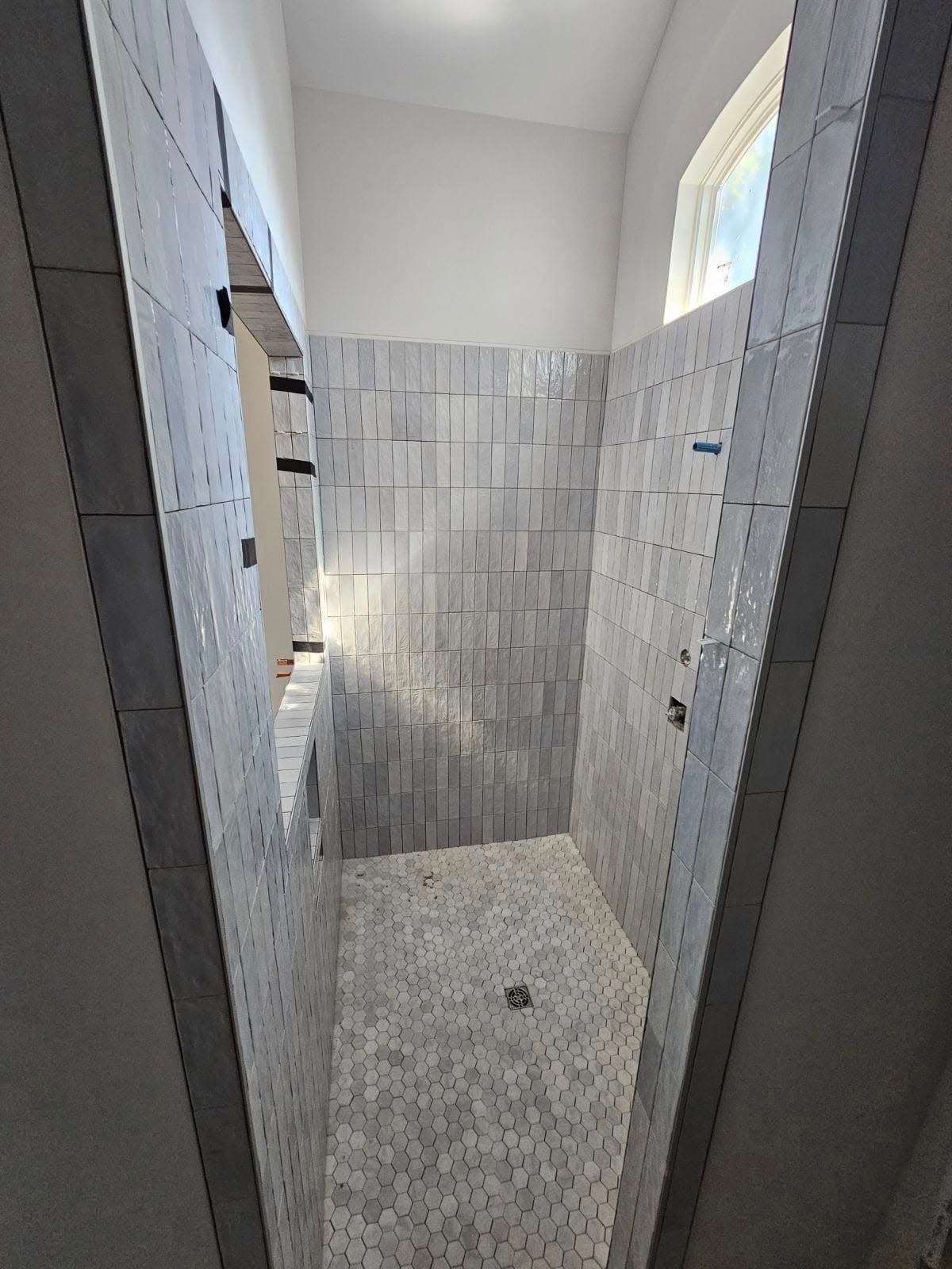 Narrow tiled shower stall with a handheld showerhead and a small high window