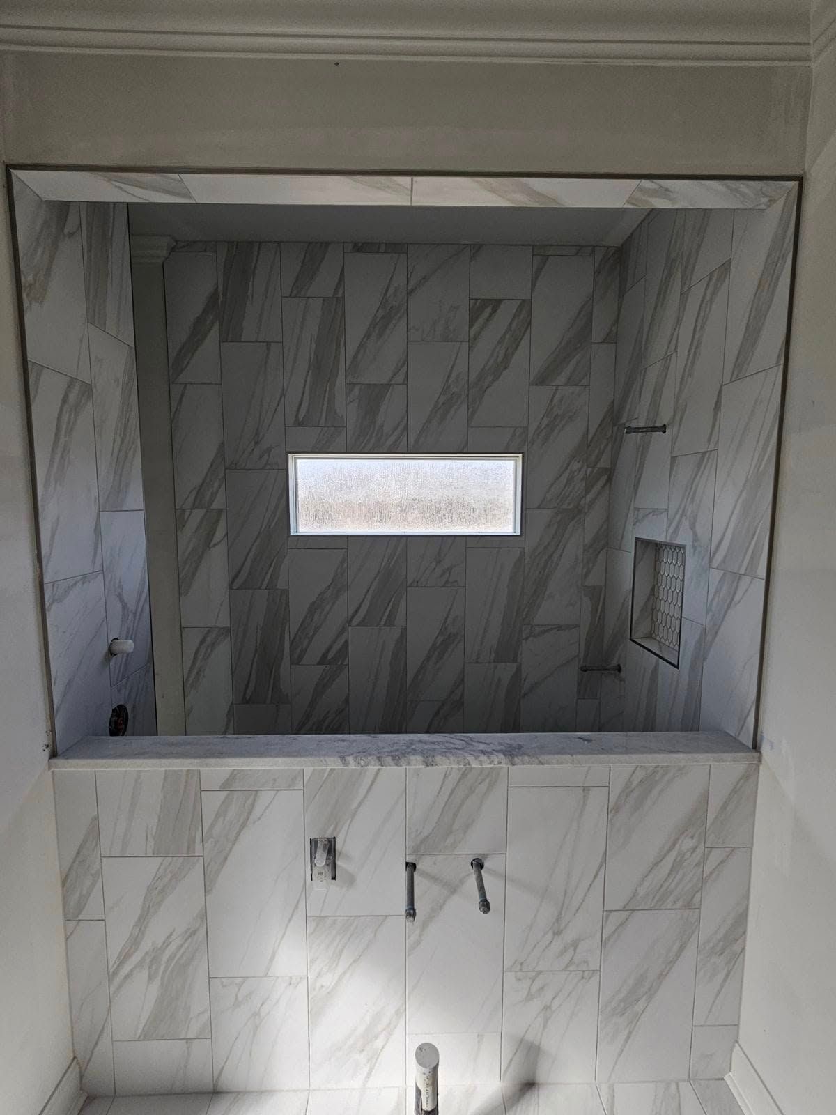 Built-in marble-tiled shower niche with small window and chrome fixtures
