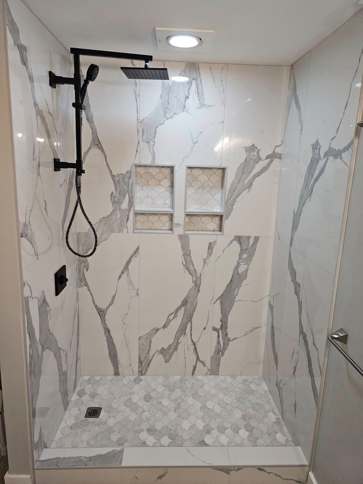 Modern shower with marble-look tile, bench seating, rain shower head, and handheld shower sprayer.