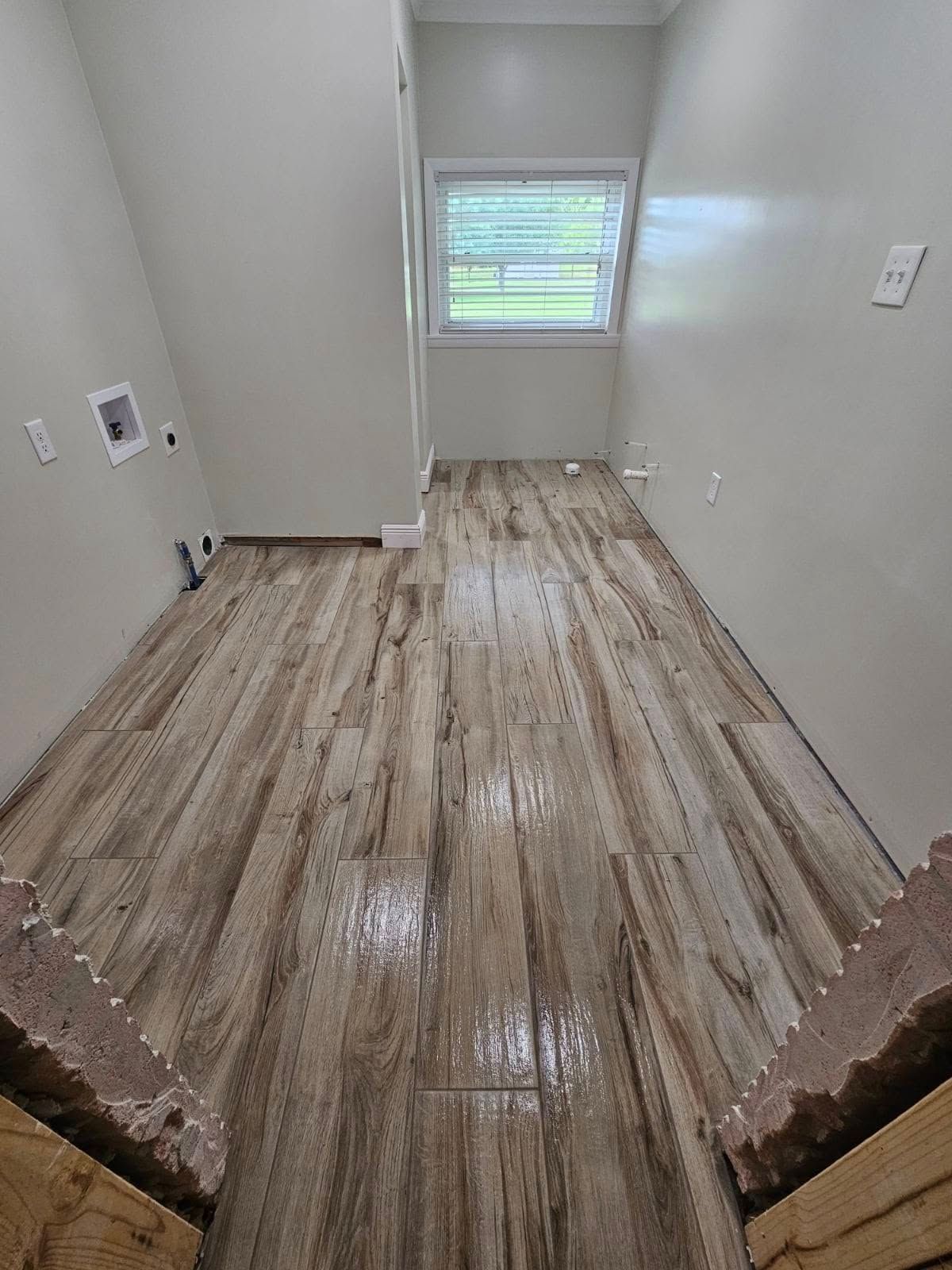 Empty room with new wood-look flooring, white walls, and a window at the far end.