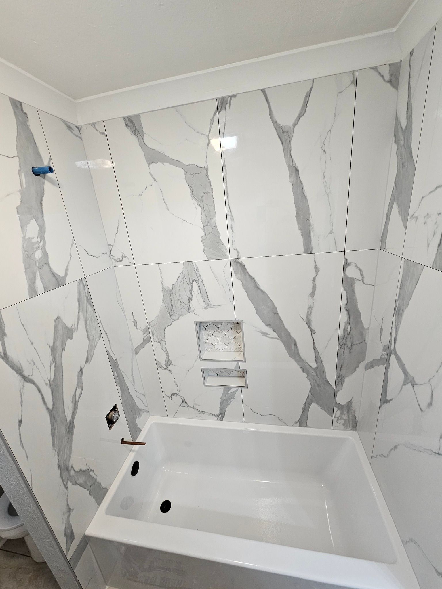 Small bathroom shower/tub alcove with gray marble-look tile and a built-in niche.