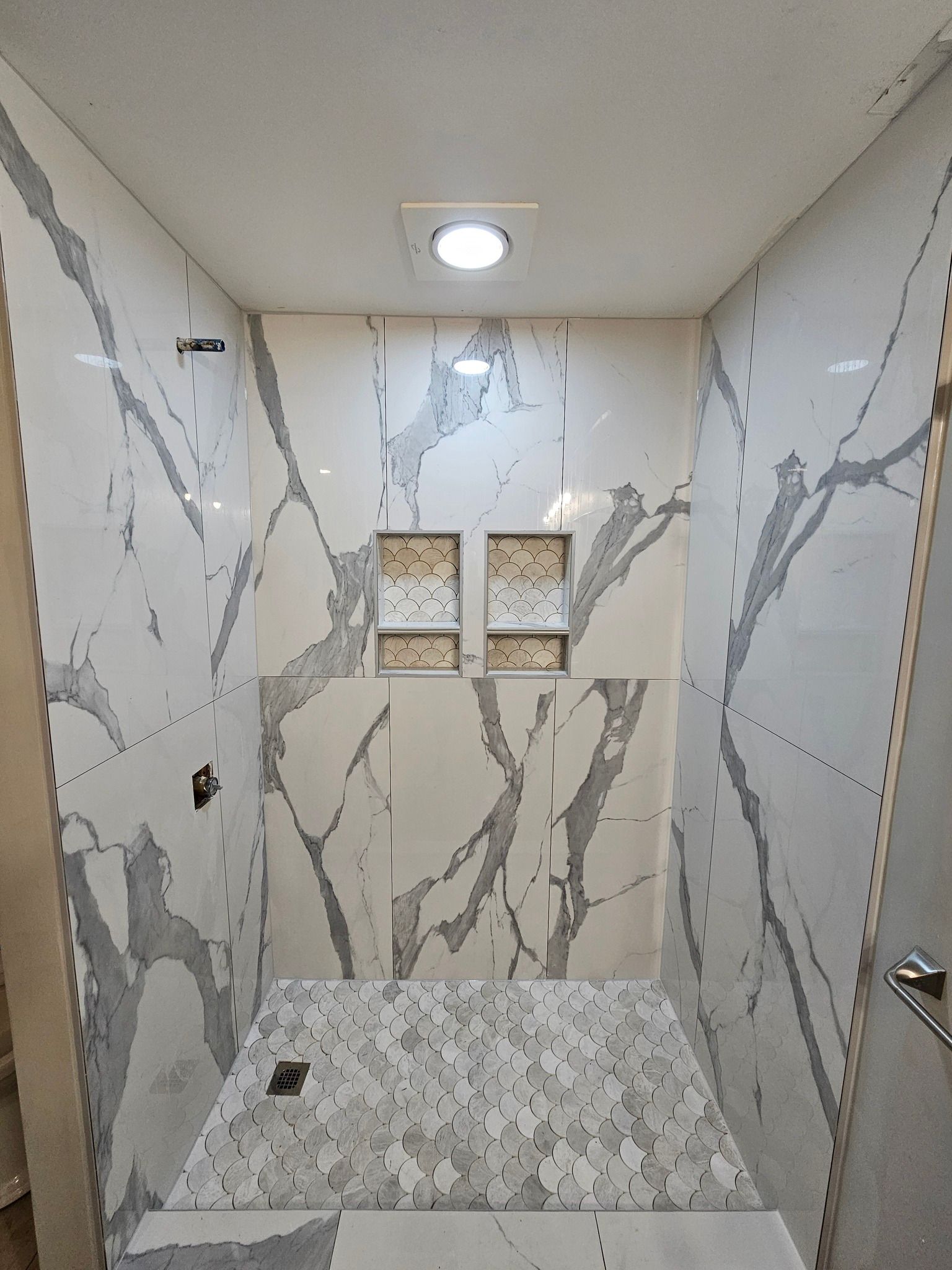 Small marble-tiled shower stall with a recessed light and two small wall niches.