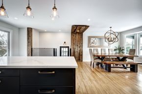 Modern kitchen and dining area with white island, wood floors, and rustic beam accents