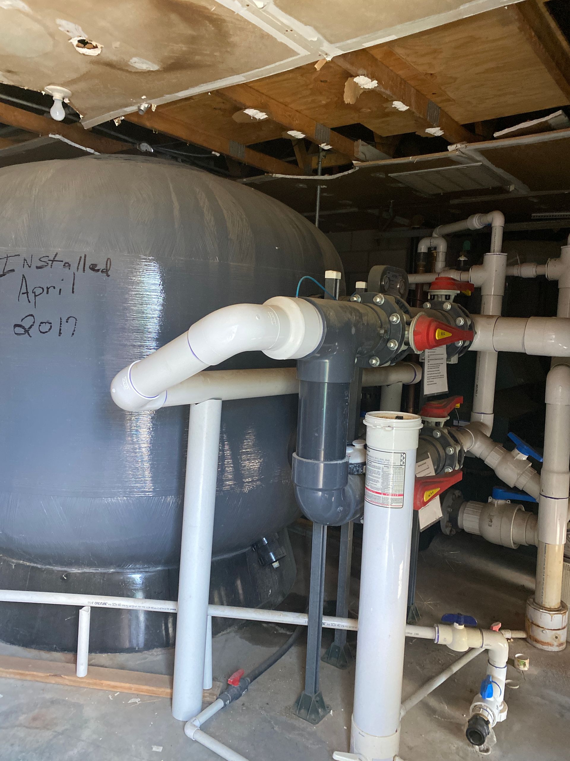 Industrial machinery with gray tank, white pipes, and valves in a basement utility room