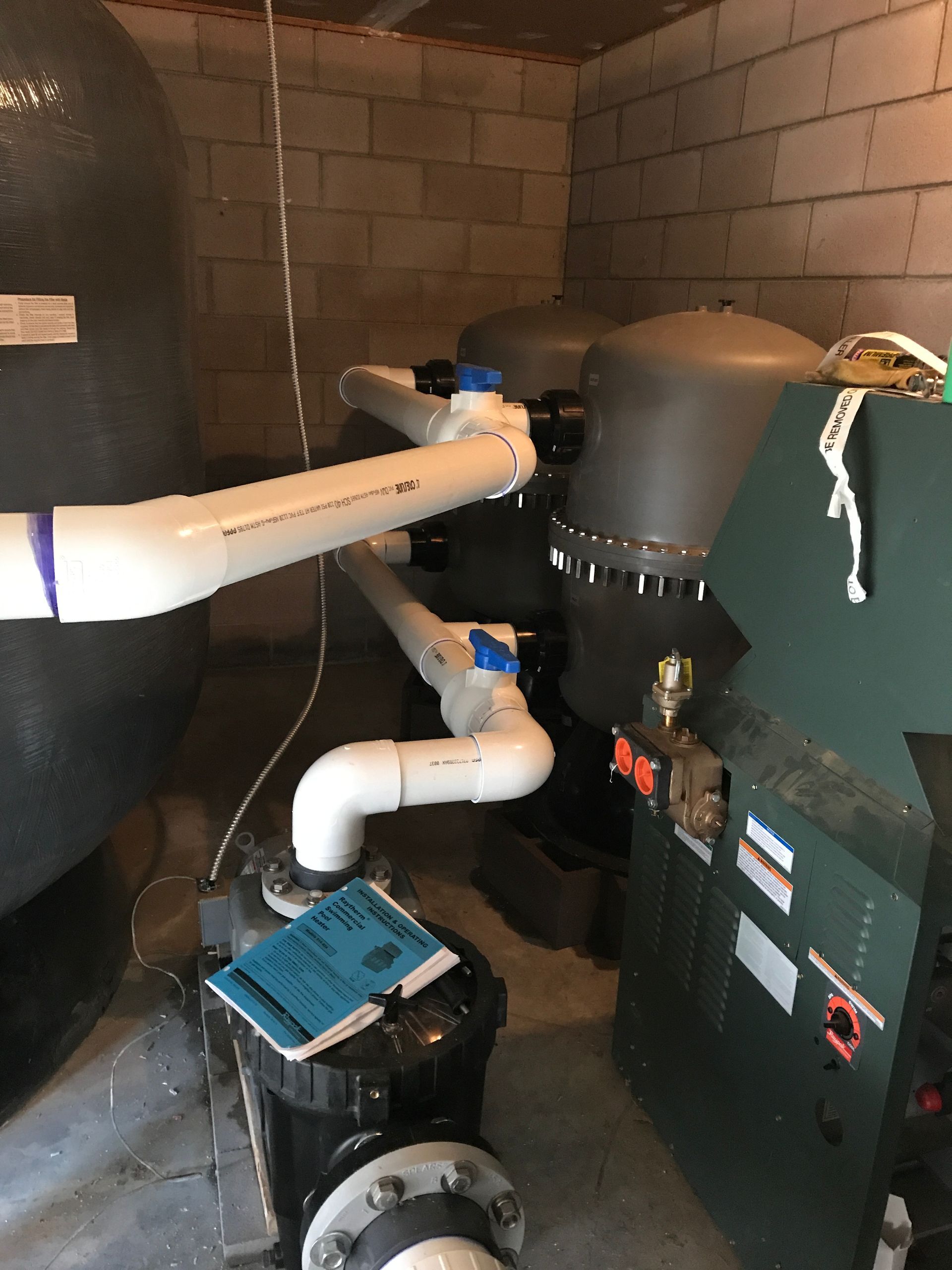 Basement mechanical room with pipes, pump, and large green and black HVAC equipment against cinderblock walls