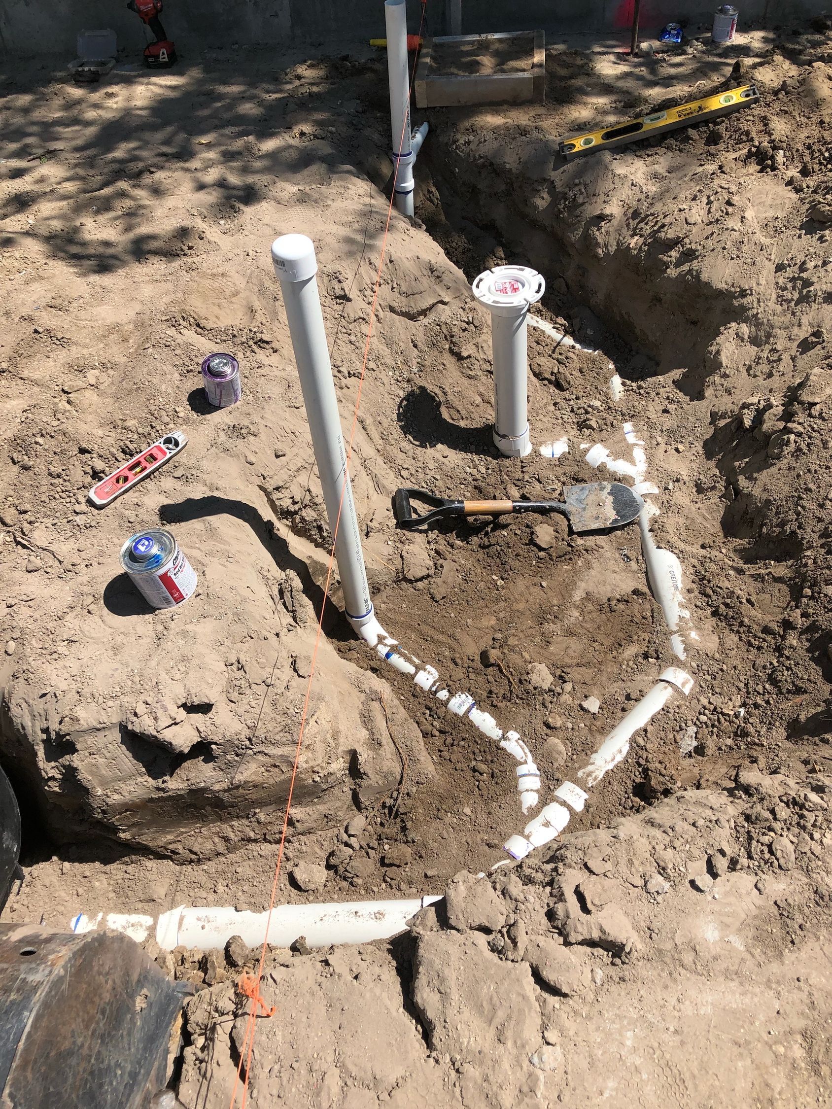 Exposed PVC pipes and valves in a dirt trench during outdoor plumbing work