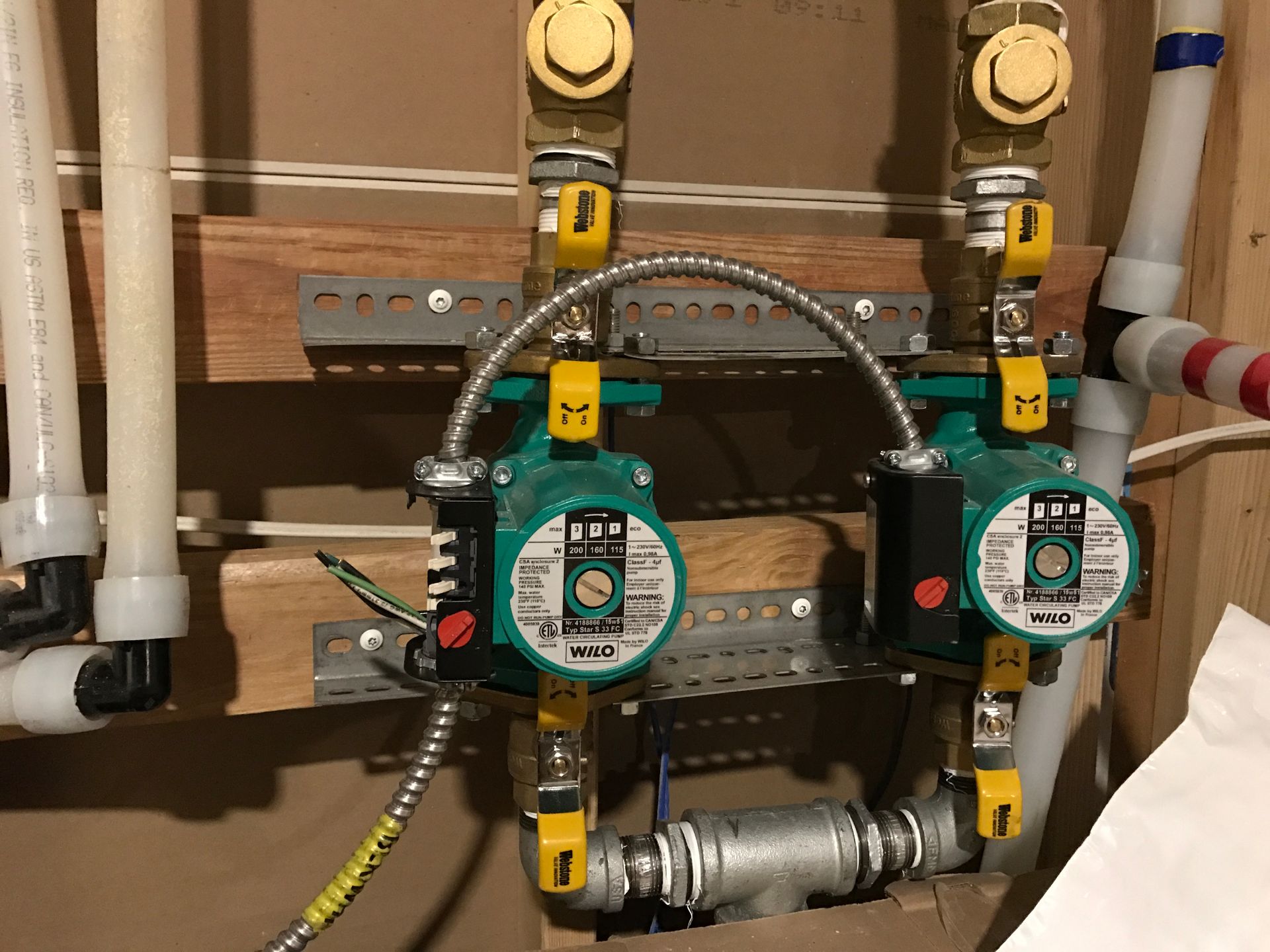 Two green pump controllers with yellow valves and piping mounted on a wooden board in a utility room