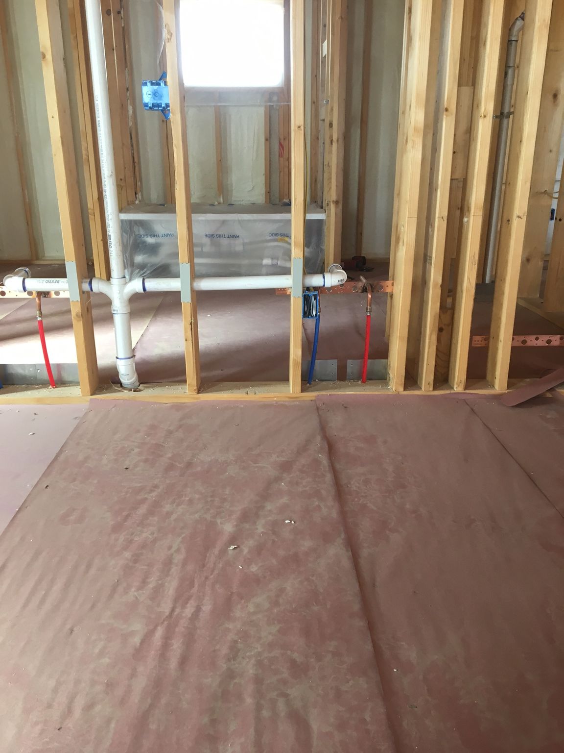 Unfinished basement with exposed wall studs, plumbing pipes, and concrete floor under construction