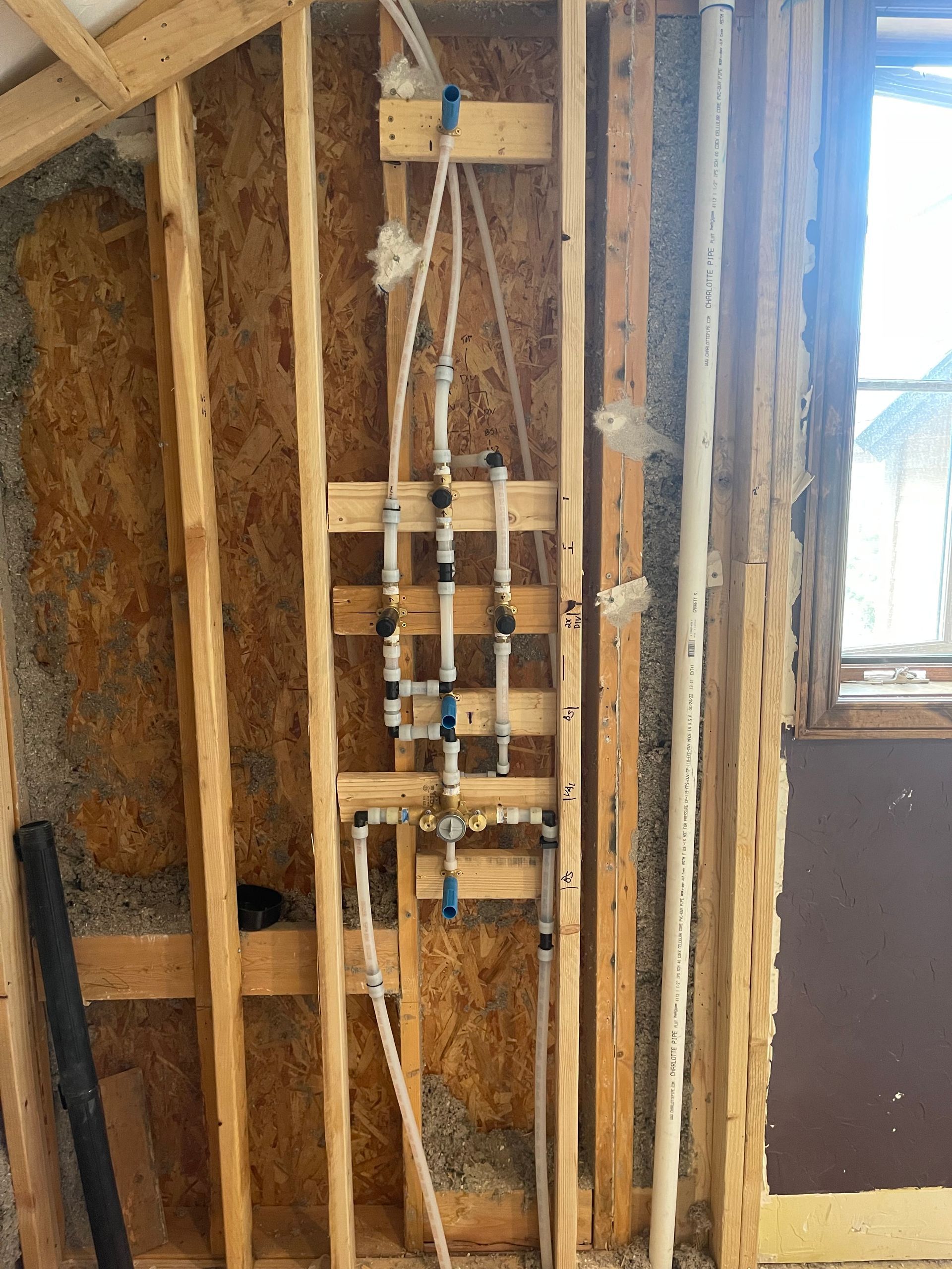 Exposed wall plumbing with pipes, valves, and wood framing in an unfinished interior
